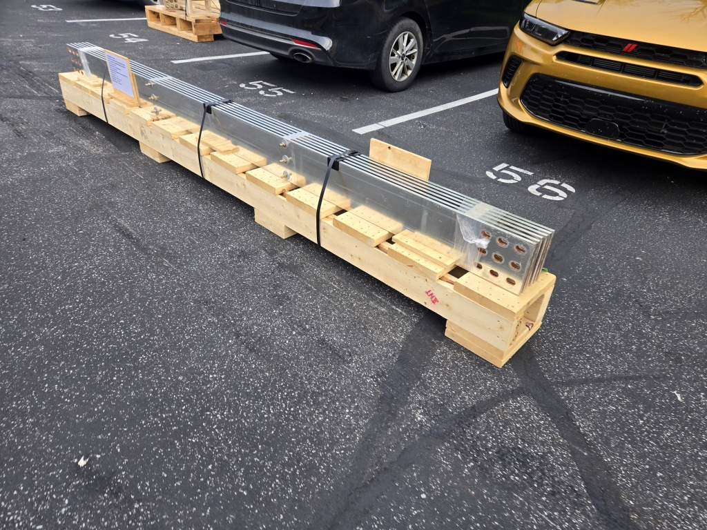 Multiple assembled bus bars are securely packed in a wooden crate and staged in a parking lot, ready for shipment to a customer.