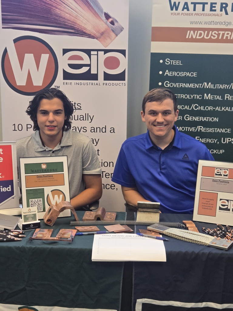 Ronald Hamm and Nicholas Chalkias representing Watteredge at their booth during the Lorain County OhioMeansJobs Job Fair, displaying copper components and recruitment materials.